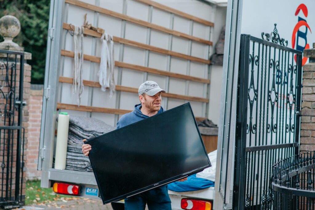 A member of the Steeles of Stamford team carrying a television from the back of a removals van